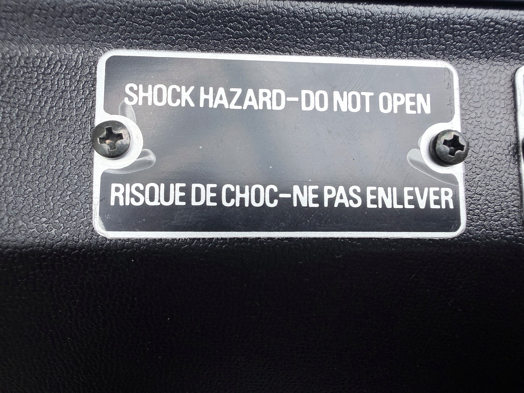 Close collection photograph of the bilingual shock-hazard plate on the Roland TR-808 underside