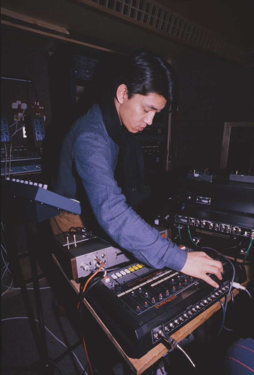 Ryuichi Sakamoto working beside a TR-808 and other equipment in a studio
